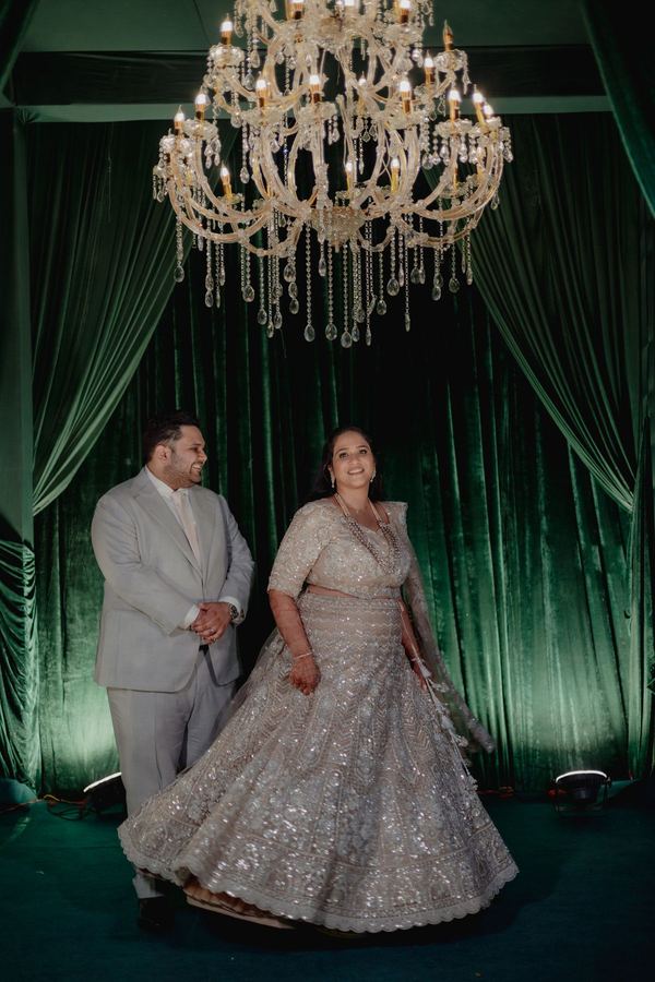 Couple beneath a crystal chandelier before green velvet drapes