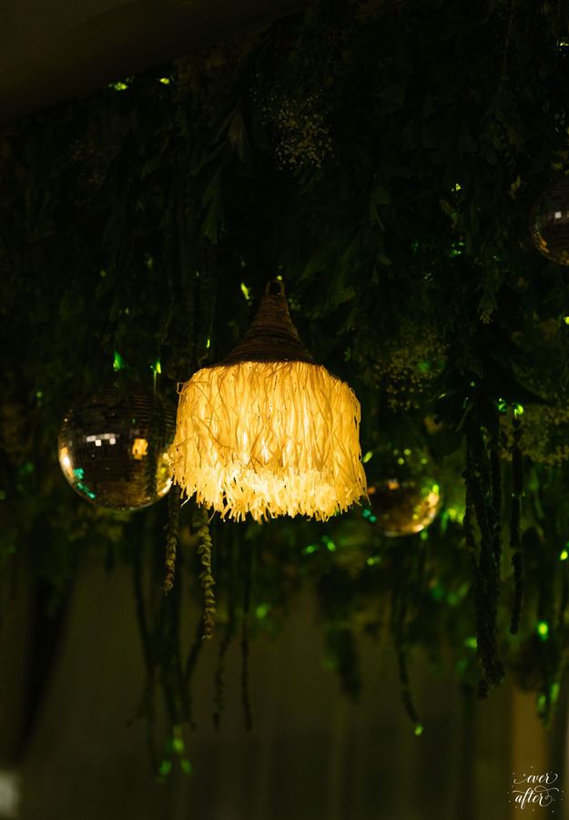 Fringed rattan lantern glowing among hanging greenery