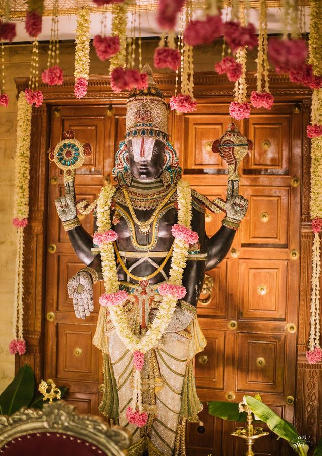 Deity idol draped in jasmine and rose garlands before a carved door