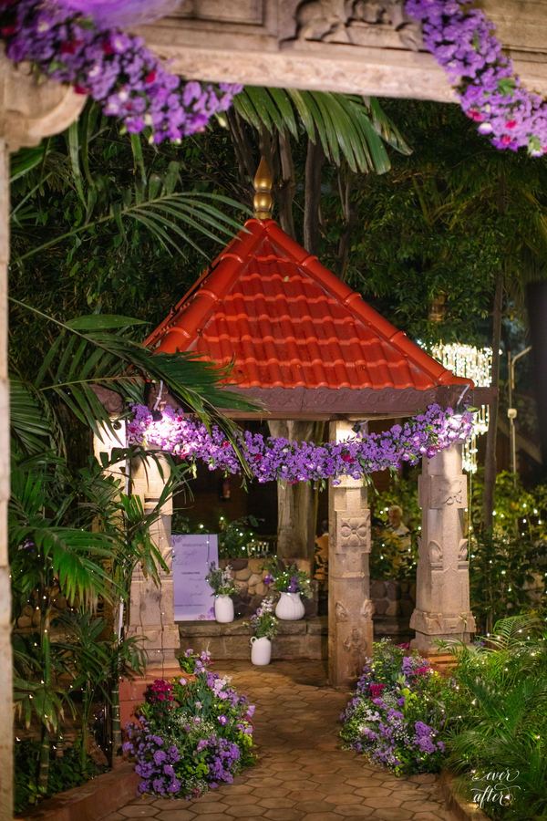 Red-roofed garden pavilion wrapped in violet flowers